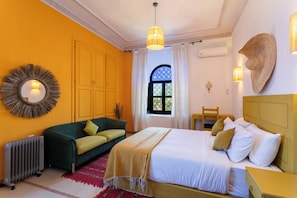 A hotel room with a bed, a sofa, a radiator, a window with curtains, and a wall-mounted mirror.