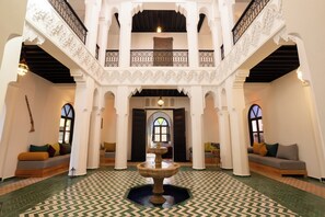 Un interior espacioso con una fuente central, columnas blancas ornamentales y un suelo con diseño.