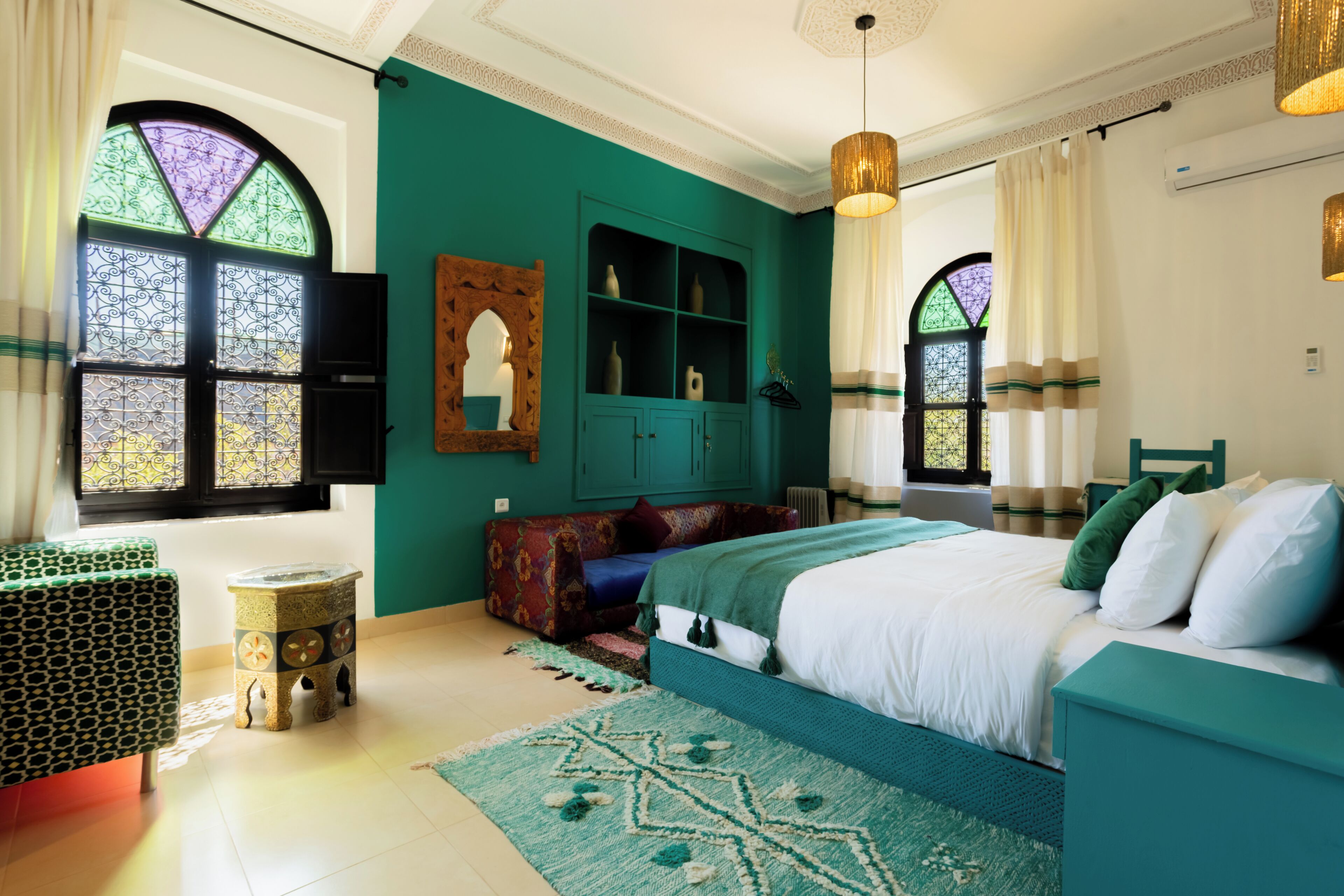 Una camera da letto con un letto, un armadietto verde, uno sgabello e una finestra con vetri decorativi.