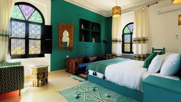 A bedroom with a bed, a green cabinet, a small stool, and a window with decorative glass.