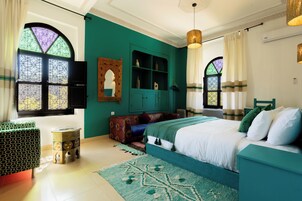 Un dormitorio con cama, un armario verde, un taburete pequeño y una ventana con vidrieras decorativas.