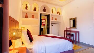 Una habitación de hotel con cama, mesita de noche, lámpara y estantes con objetos decorativos.