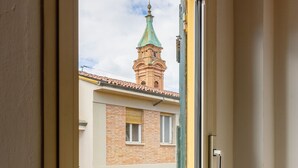 Ein Fenster mit Blick auf ein Gebäude mit einer grünen Turmspitze und einem Balkon mit aufwendiger Eisenverzierungen.