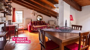 Ein gemütliches Zimmer mit Holzbalkendecke, einem roten Sofa, einem Esstisch und einem Stuhl.