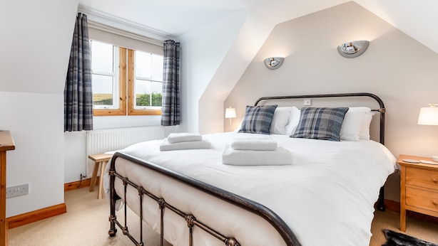 Ein Schlafzimmer mit Bett, Nachttisch, Lampe und einem Fenster mit Vorhängen.