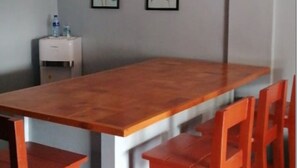 A room with a wooden table and red chairs, a small white side table with a water bottle, and two framed pictures on the wall. - Duplex beach house (Calabarzon)