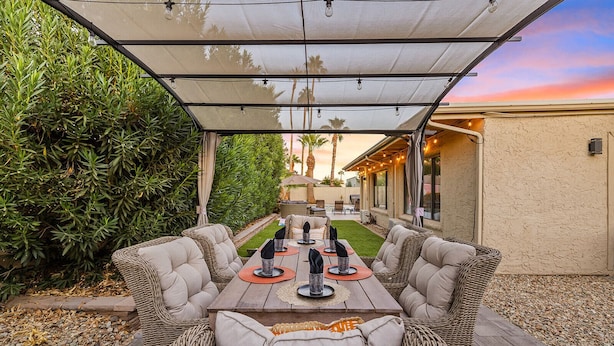 An outdoor patio with a covered dining table, wicker chairs, and a view of the house in the background. - Desert Legacy | Scottsdale's Hidden Hideaway (Scottsdale)