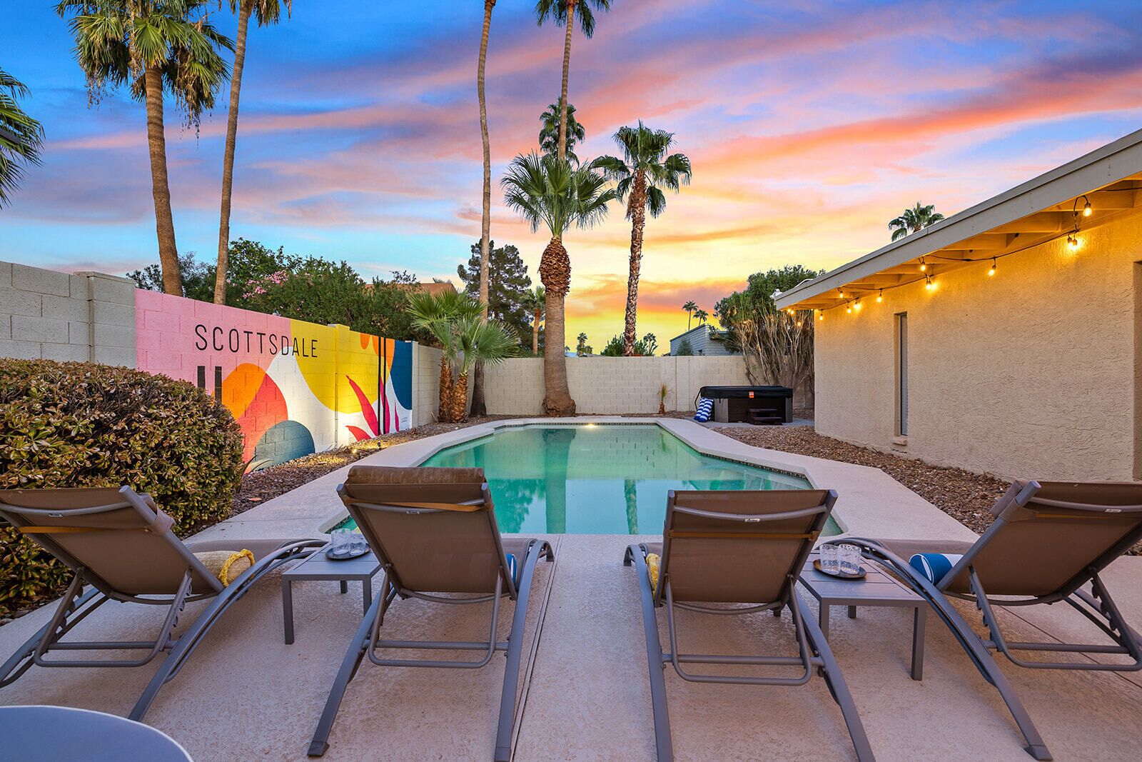 A pool area with lounge chairs, a colorful mural, and palm trees.