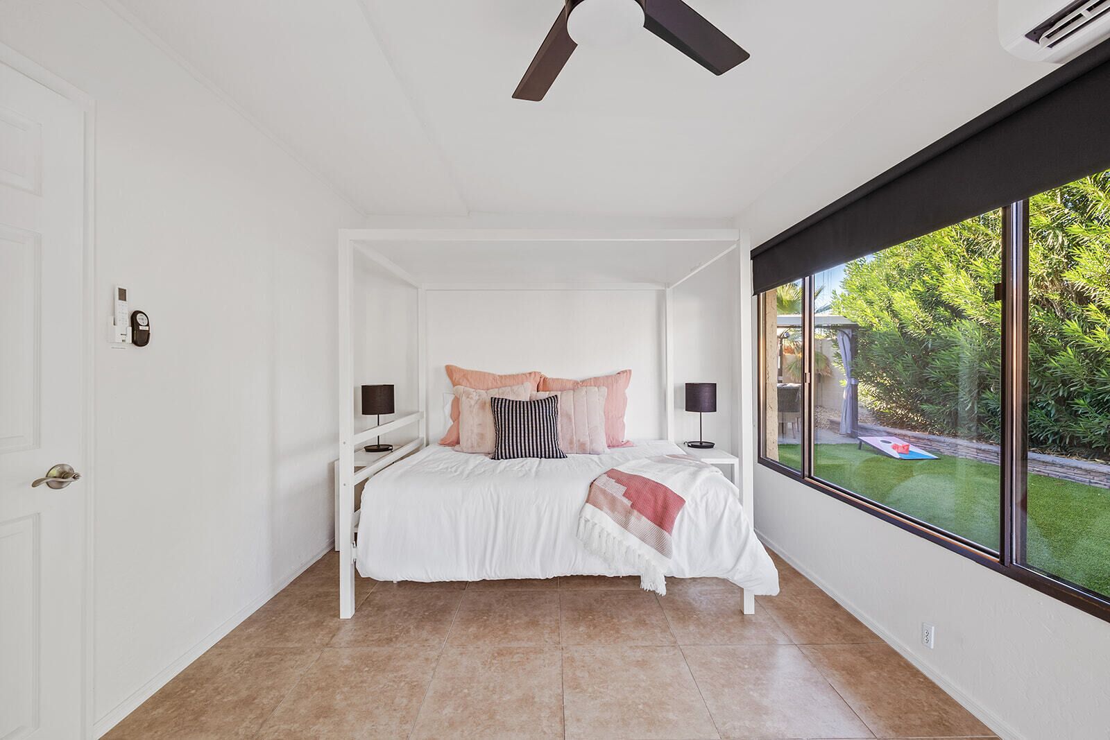 Ein Schlafzimmer mit einem Bett, Nachttischen, einem Deckenventilator und einem großen Fenster mit Blick auf Grünflächen.