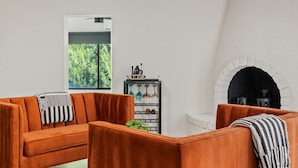 A living room with a sofa and armchairs, a fireplace, a wine rack, and a window with a view of greenery. - Desert Legacy | Scottsdale's Hidden Hideaway (Scottsdale)