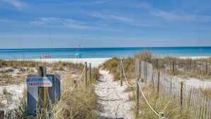 Un sentier menant à la plage, avec un panneau indiquant qu’il n’y a pas de sauveteur en service et conseillant de se baigner à ses propres risques.