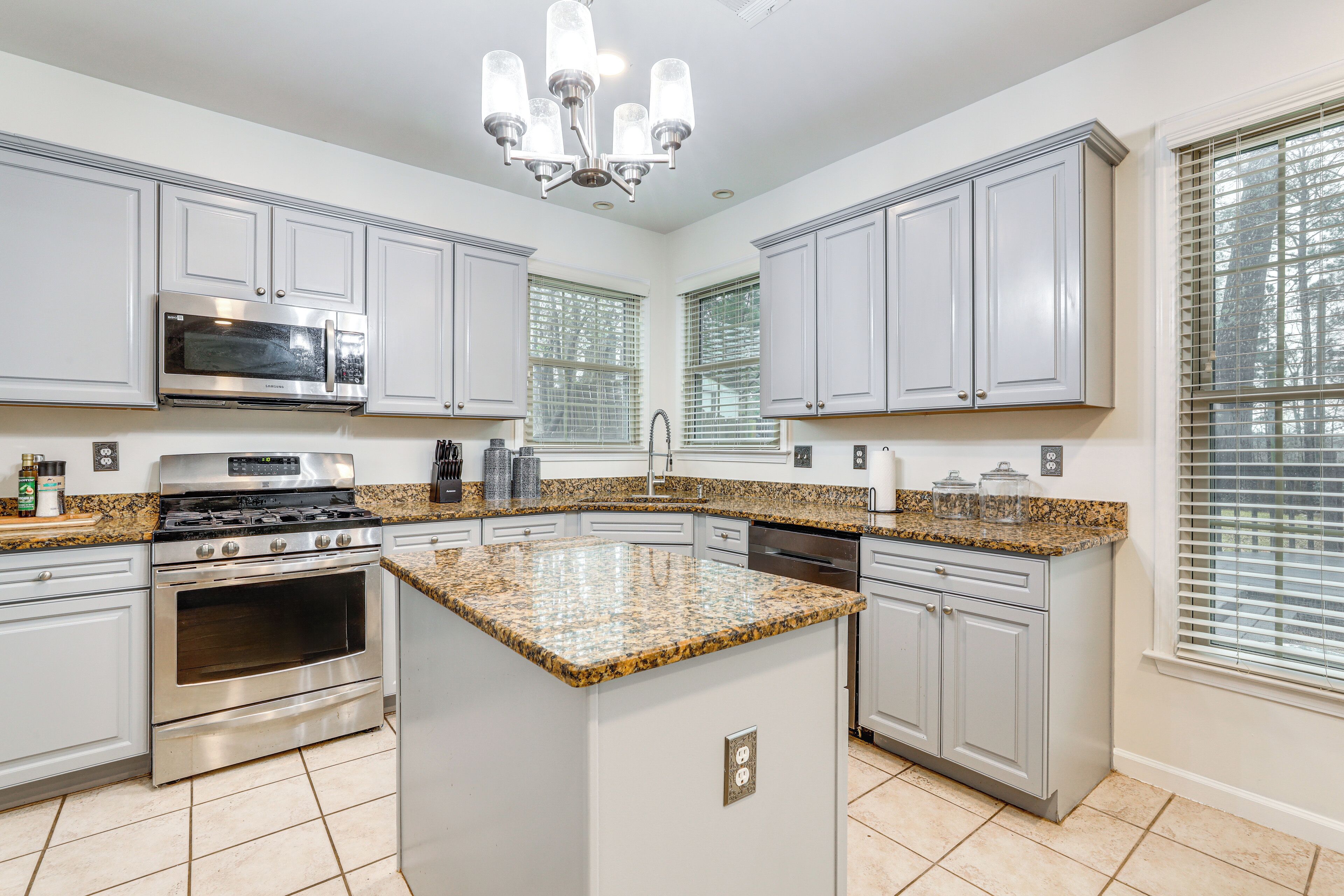 A modern kitchen with white cabinets, granite countertops, stainless steel appliances, and a central island.