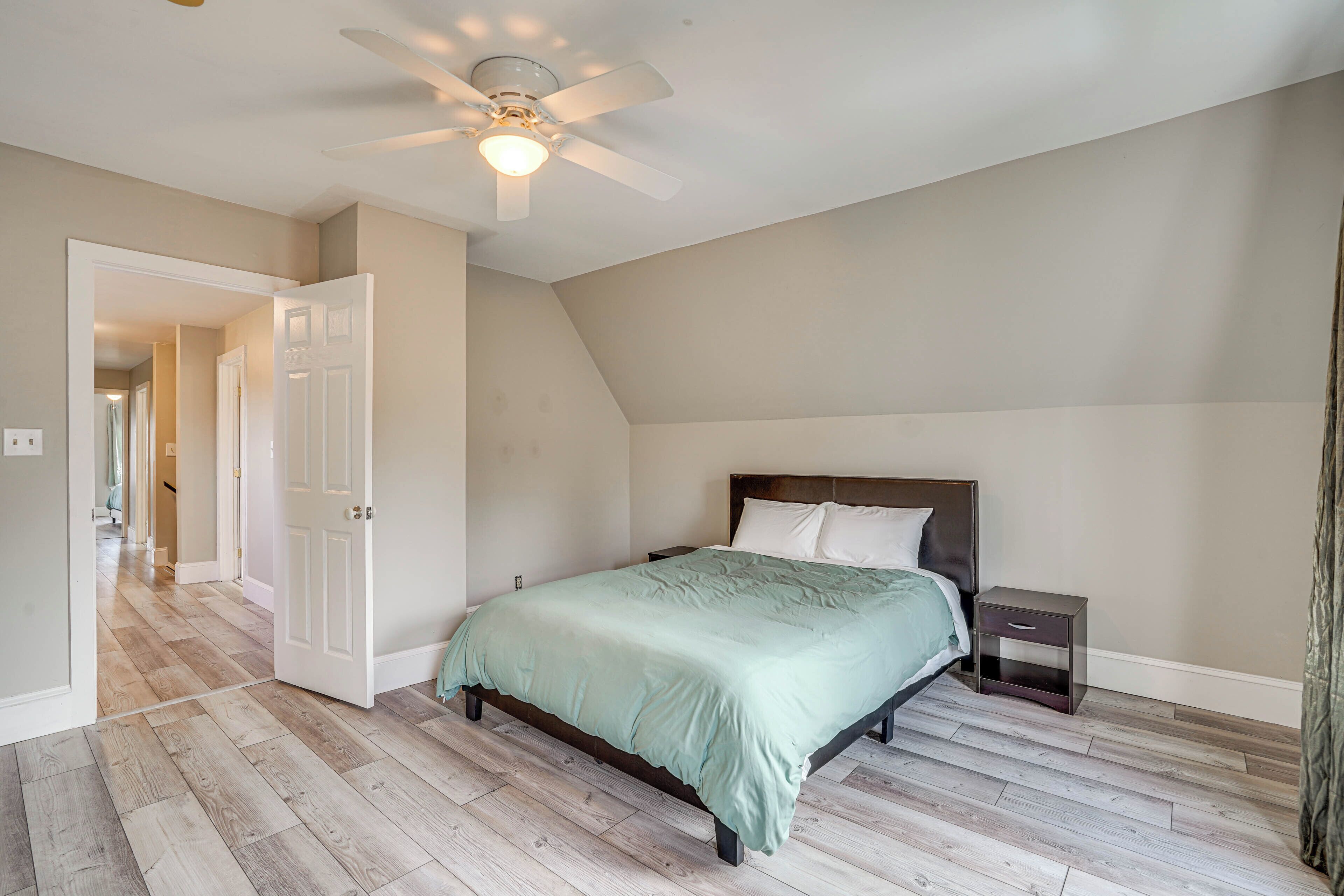 A bedroom with a bed, a nightstand, a ceiling fan, and a door leading to another room.