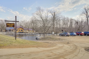 A riverside area with a sign for a salmon river fly fishing launch, a wooden cabin, and parked cars.