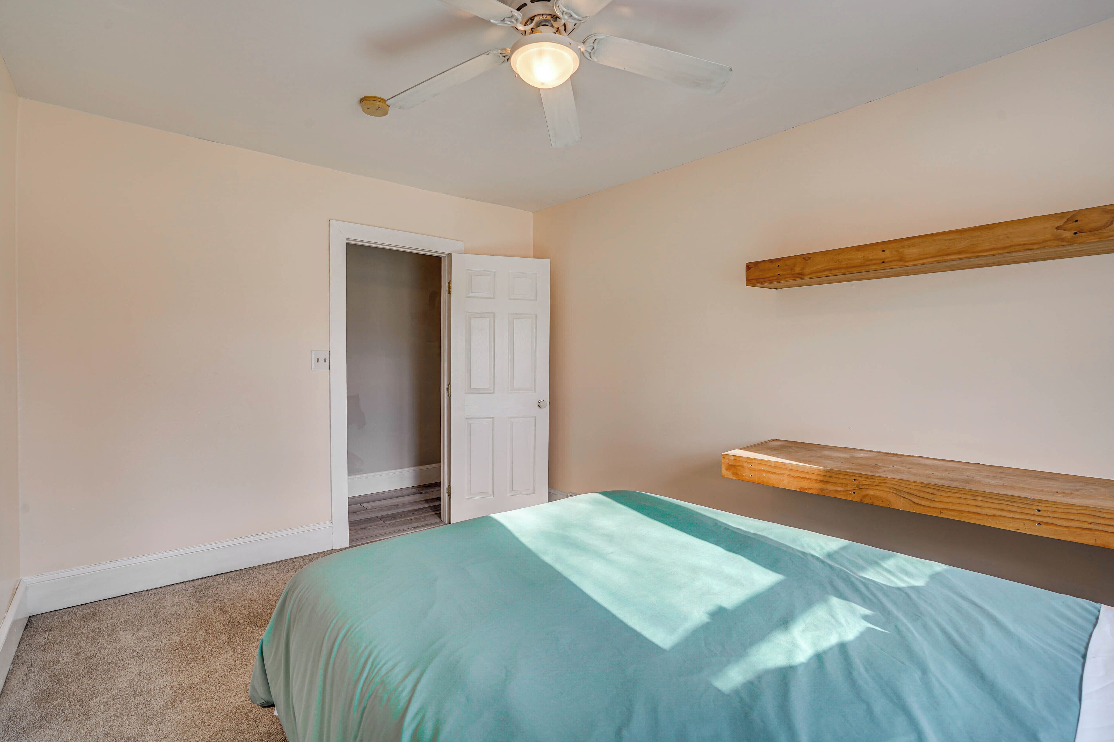 A bedroom with a bed, a ceiling fan, a door, and a wooden shelf.