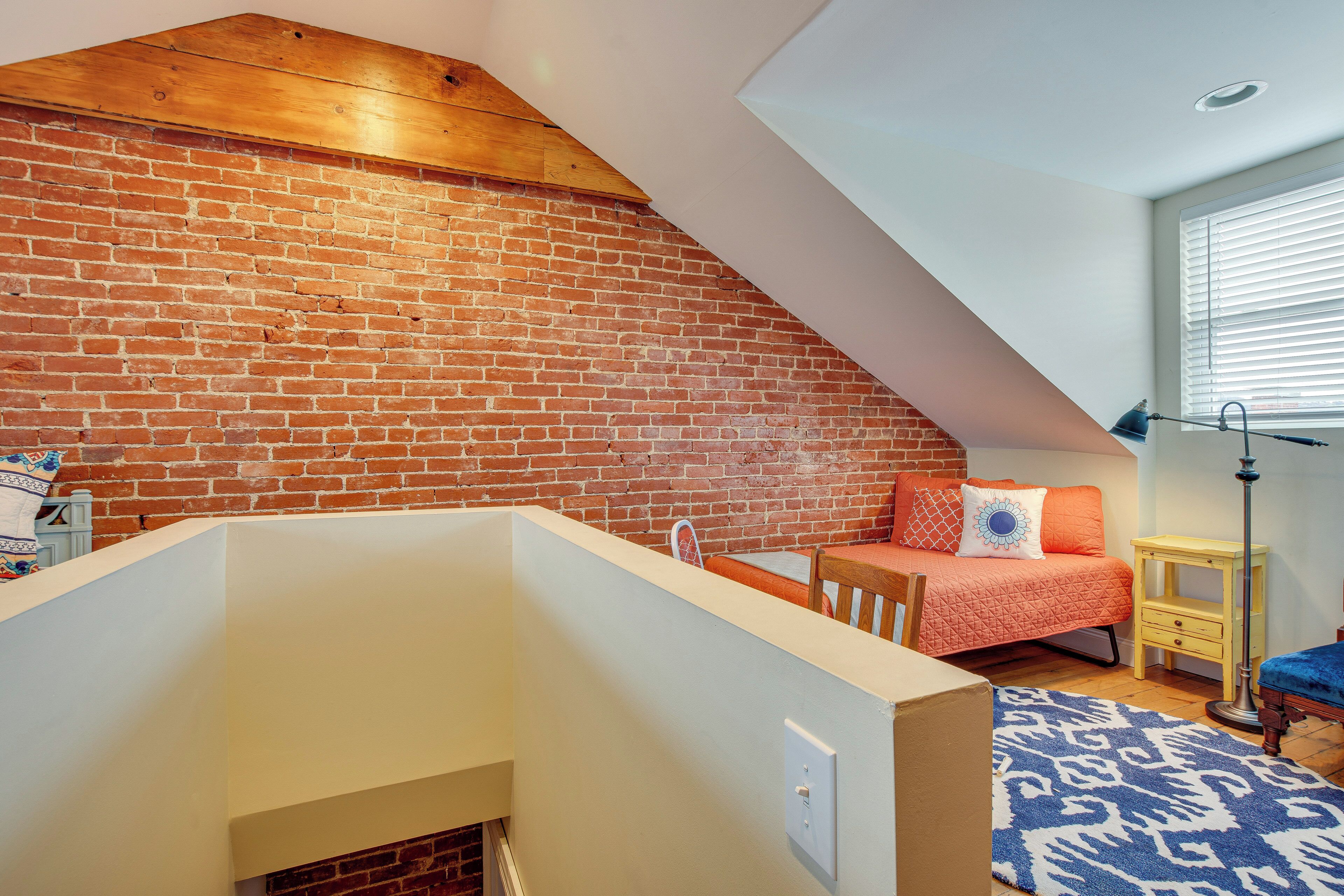 A bedroom with a sloped ceiling, brick wall, and a bed with orange bedding.
