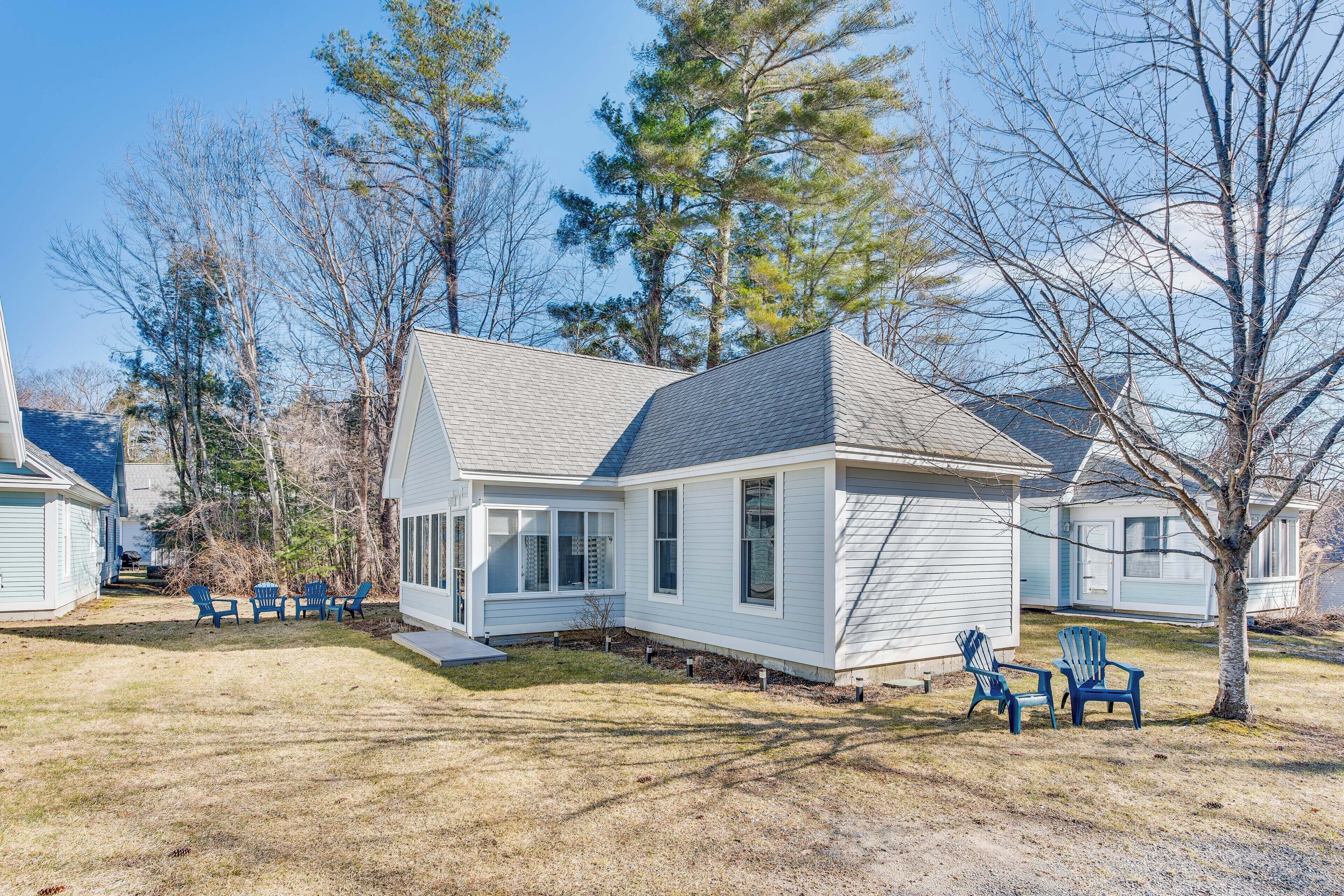 A single-story house with a gabled roof, a front porch with a railing, and a small front yard with two Adirondack chairs.