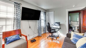 A living room with a wooden floor, a sofa, a chair, a desk with a computer, and a TV mounted on the wall. - Pet-friendly Ellenville Apartment in the Catskills (Ellenville)