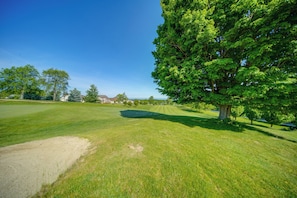 En golfbane med et stort træ, et sandbunker og en klar blå himmel.