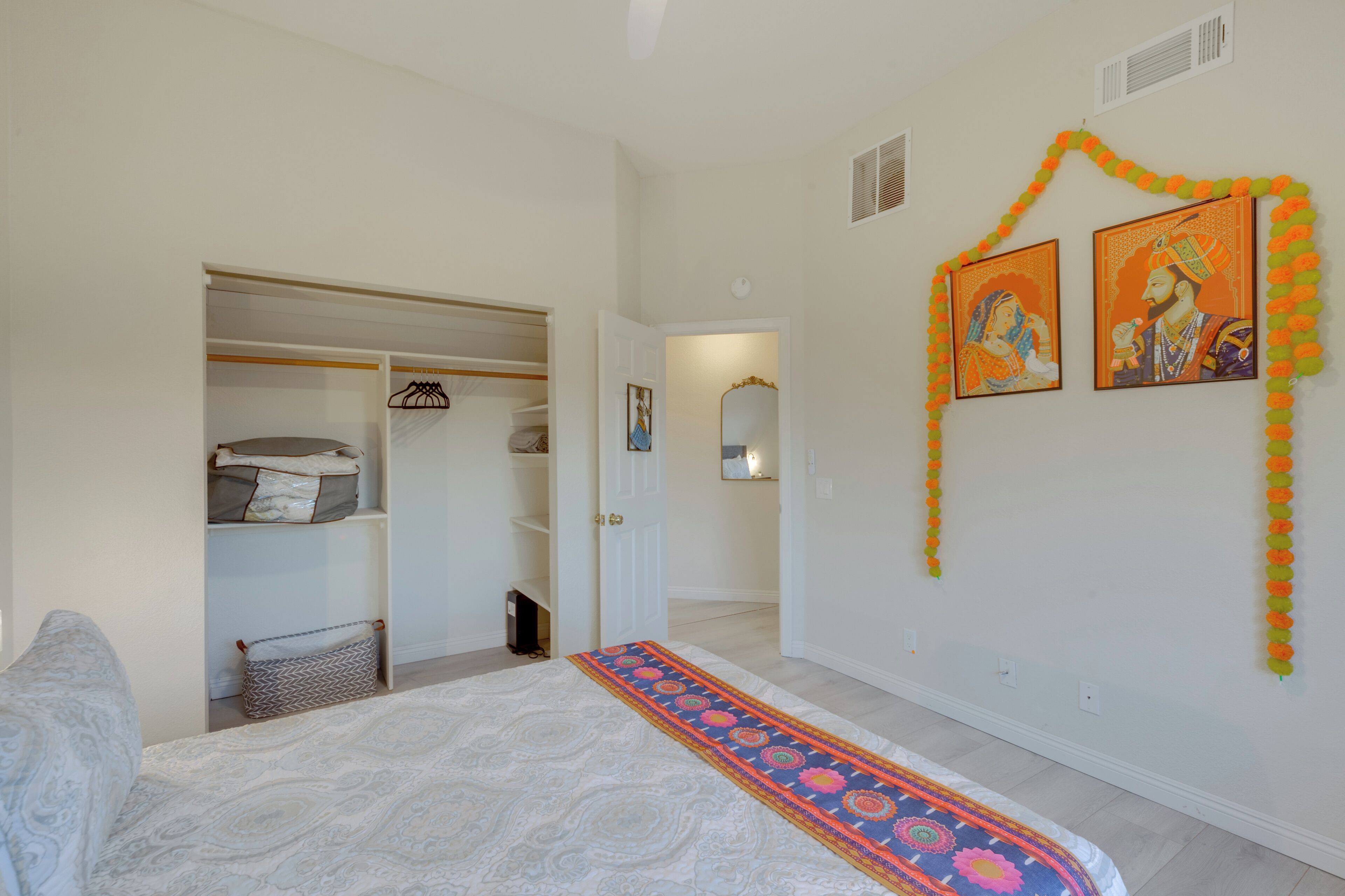 A bedroom with a bed, a wardrobe, a hallway, and a wall decorated with artwork and garlands.