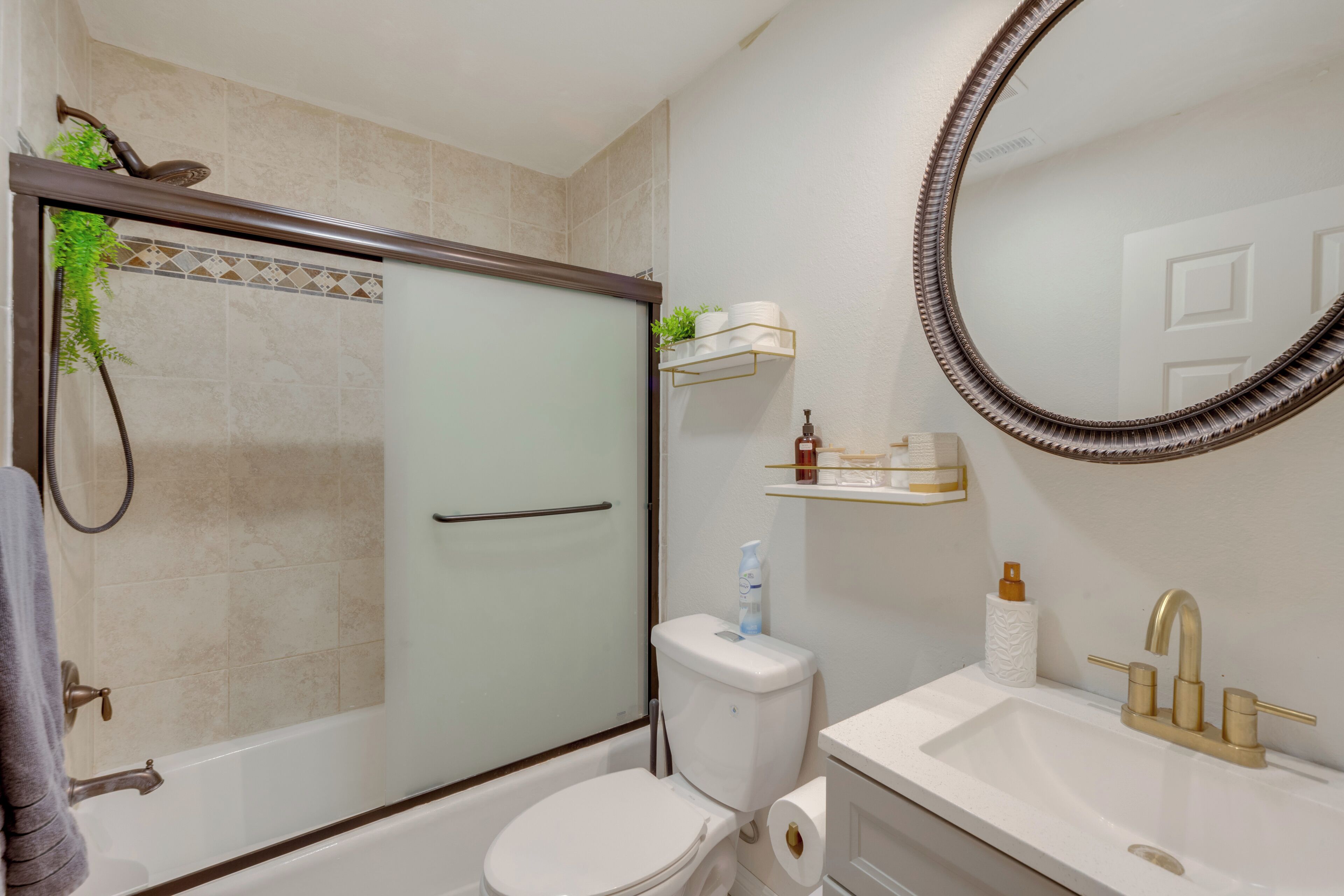 A modern bathroom with a glass-enclosed shower, a white toilet, and a sink with gold fixtures.