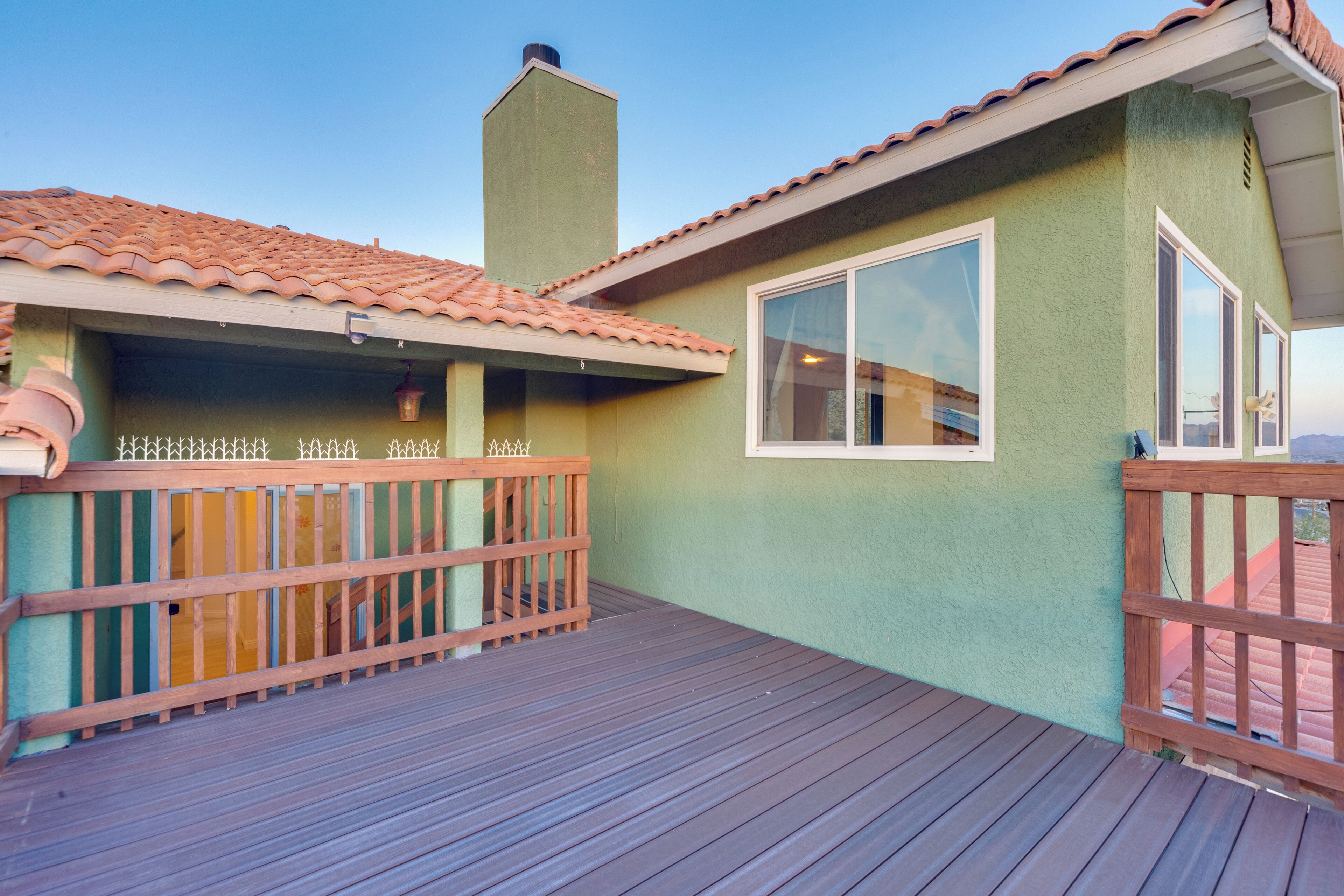 A wooden deck with a railing, a green building with a tiled roof, and a chimney.
