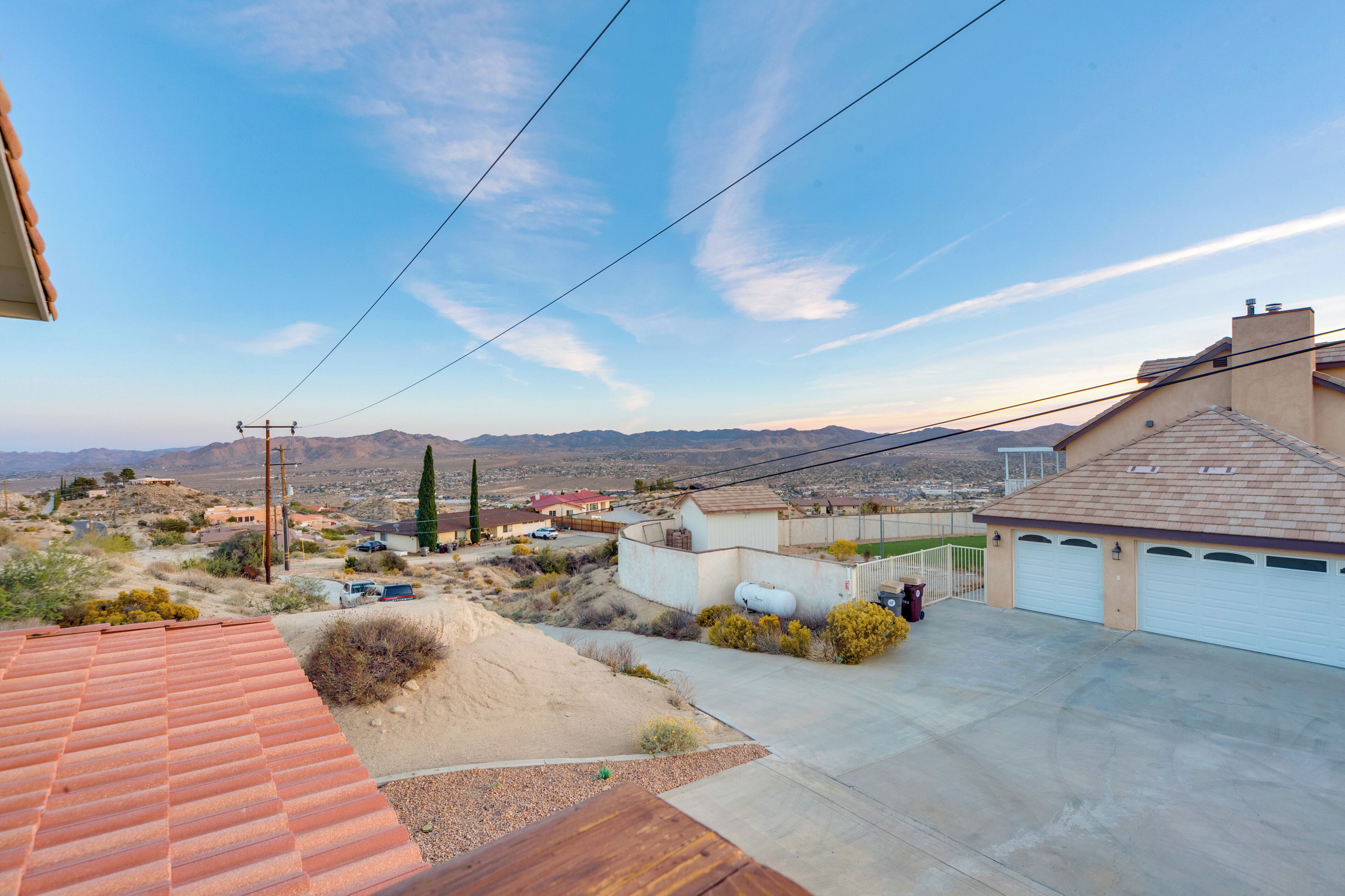 Un barrio residencial con garaje, una casa con techo rojo y una vista despejada de montañas distantes.