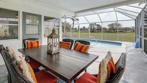 A covered patio with a wooden table and wicker chairs, overlooking a swimming pool and a grassy area. - Centrally Located Sarasota Home w/ Heated Pool! (Sarasota)