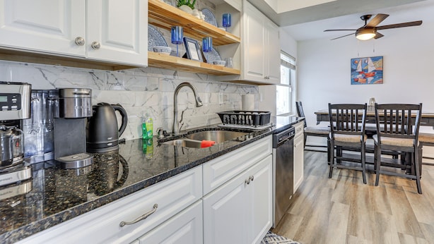 A kitchen with white cabinets, a marble backsplash, and a black countertop. There is a coffee maker, a kettle, and a toaster on the counter. - Centrally Located Sarasota Home w/ Heated Pool! (Sarasota)