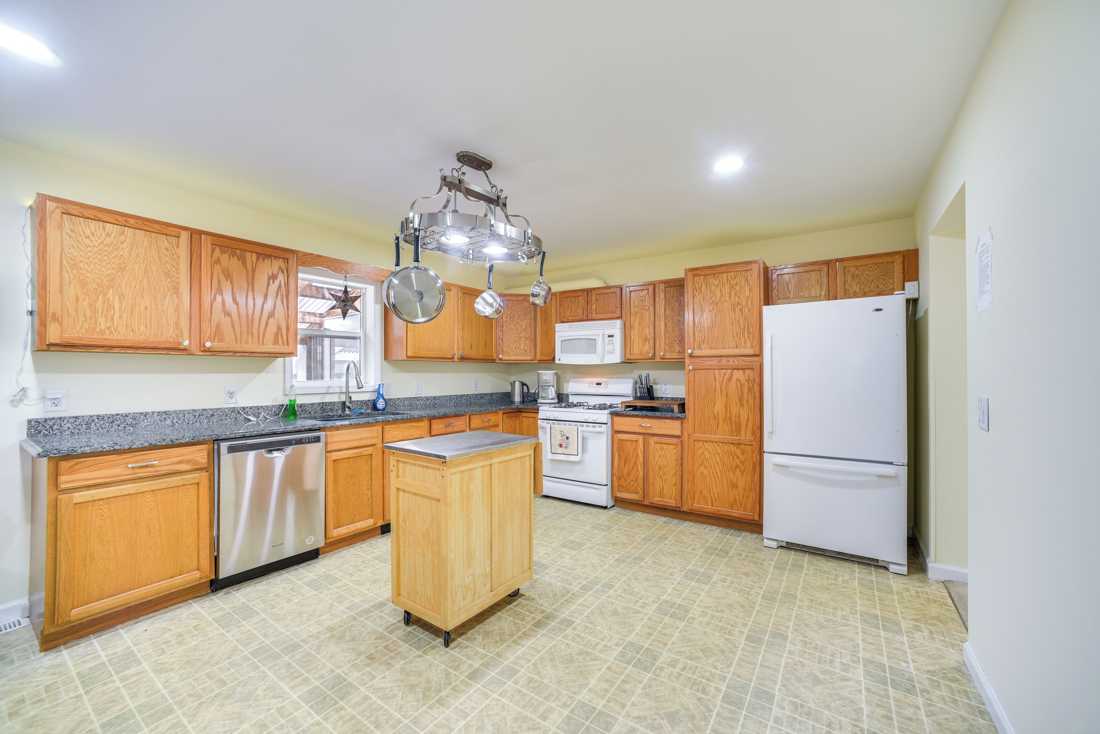 A kitchen with wooden cabinets, a central island, stainless steel appliances, and a tiled floor.