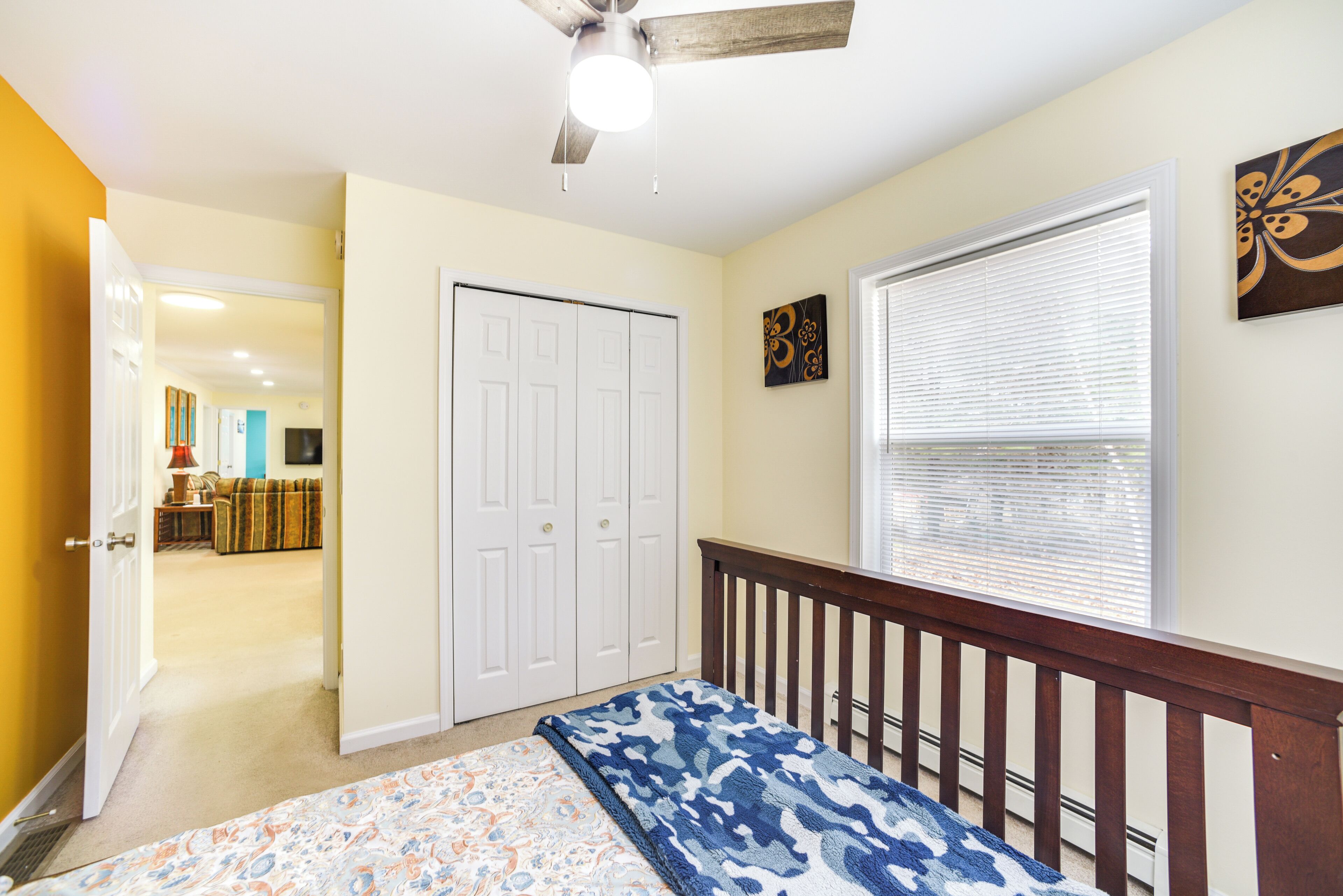 A bedroom with a bed, a ceiling fan, a window with blinds, and a door leading to another room.