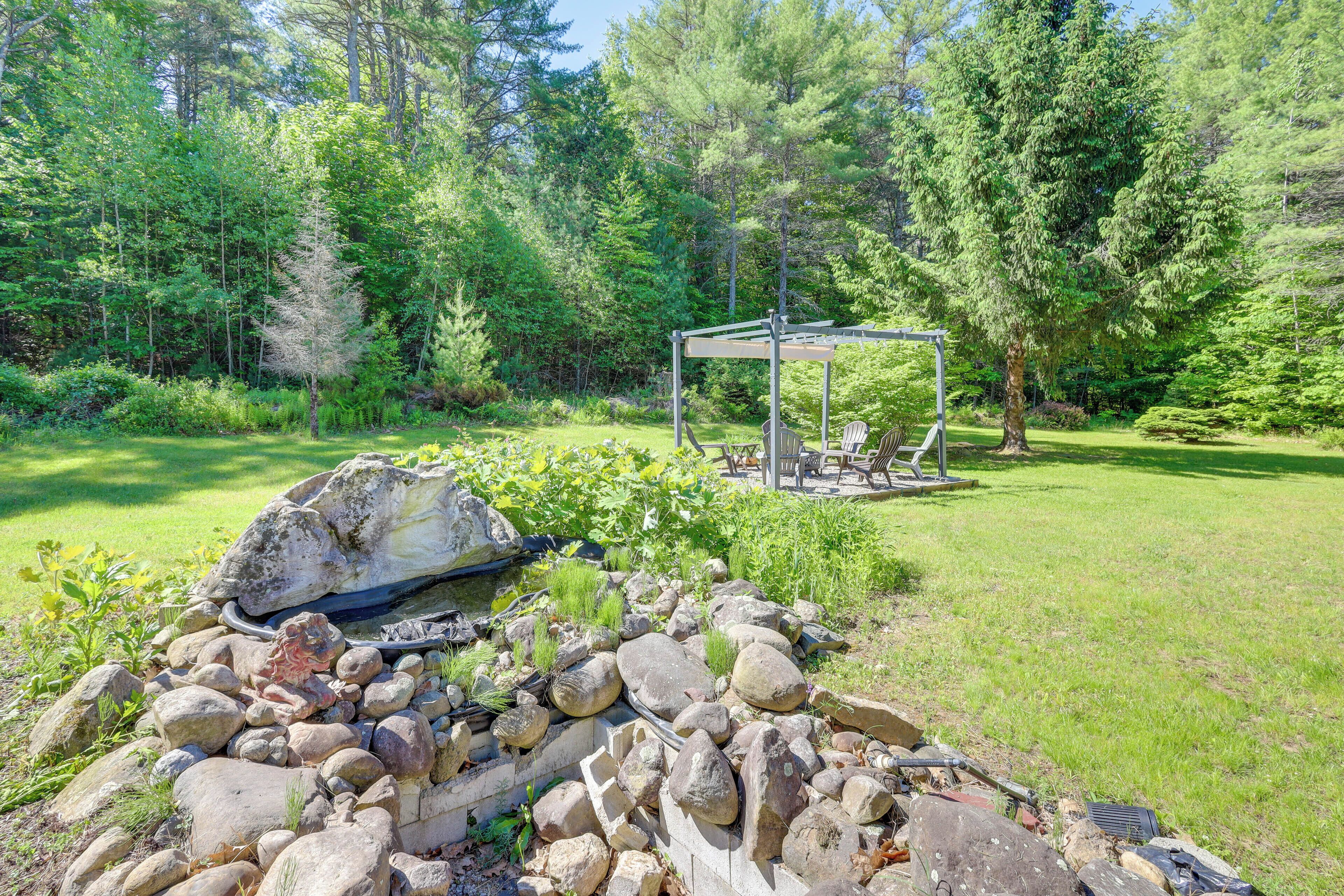 A garden with a stone fire pit, a pergola, and surrounding greenery.