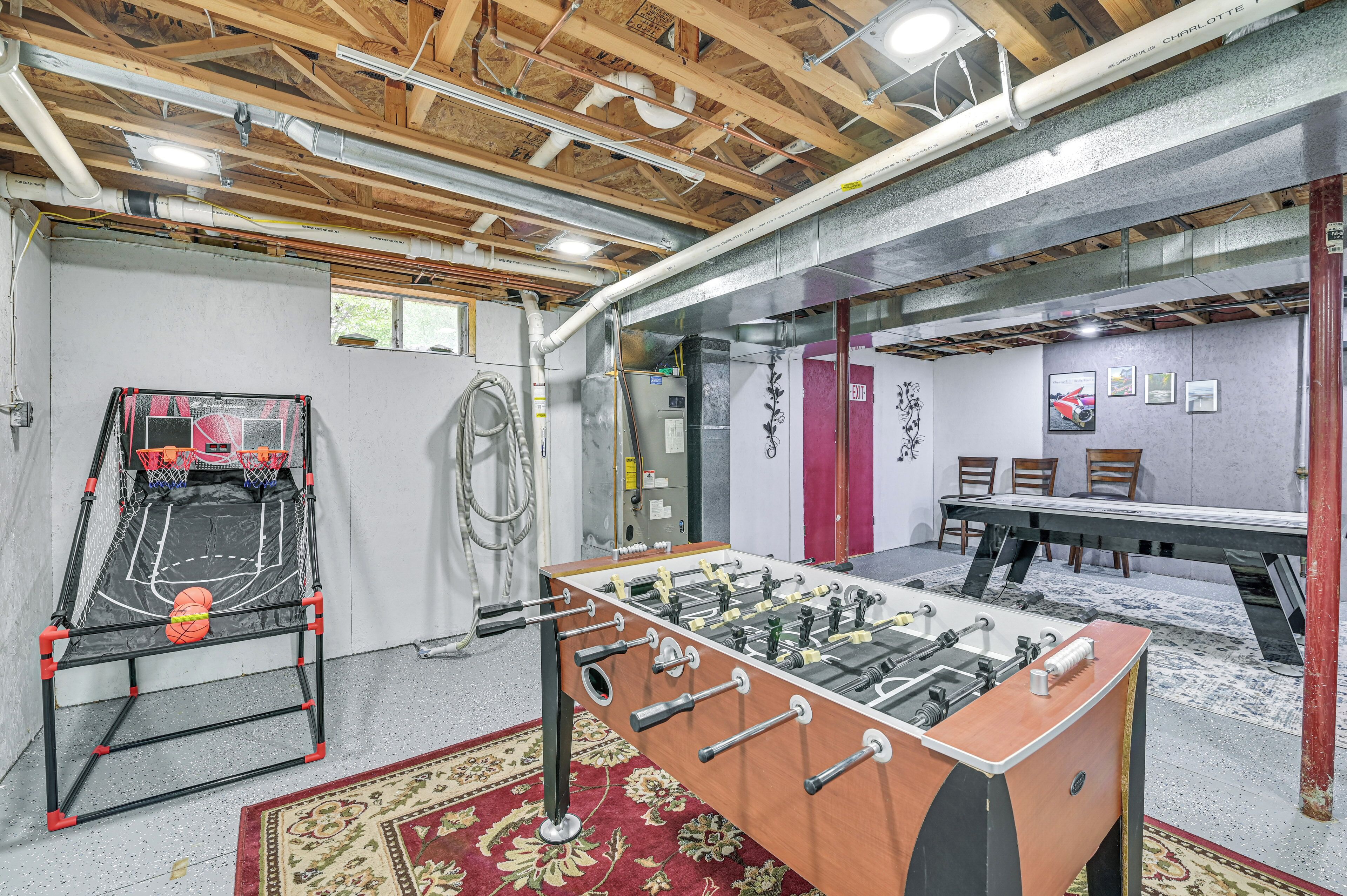A room with a foosball table, a basketball hoop, and a table tennis table.