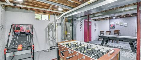 A room with a foosball table, a basketball hoop, and a table tennis table.