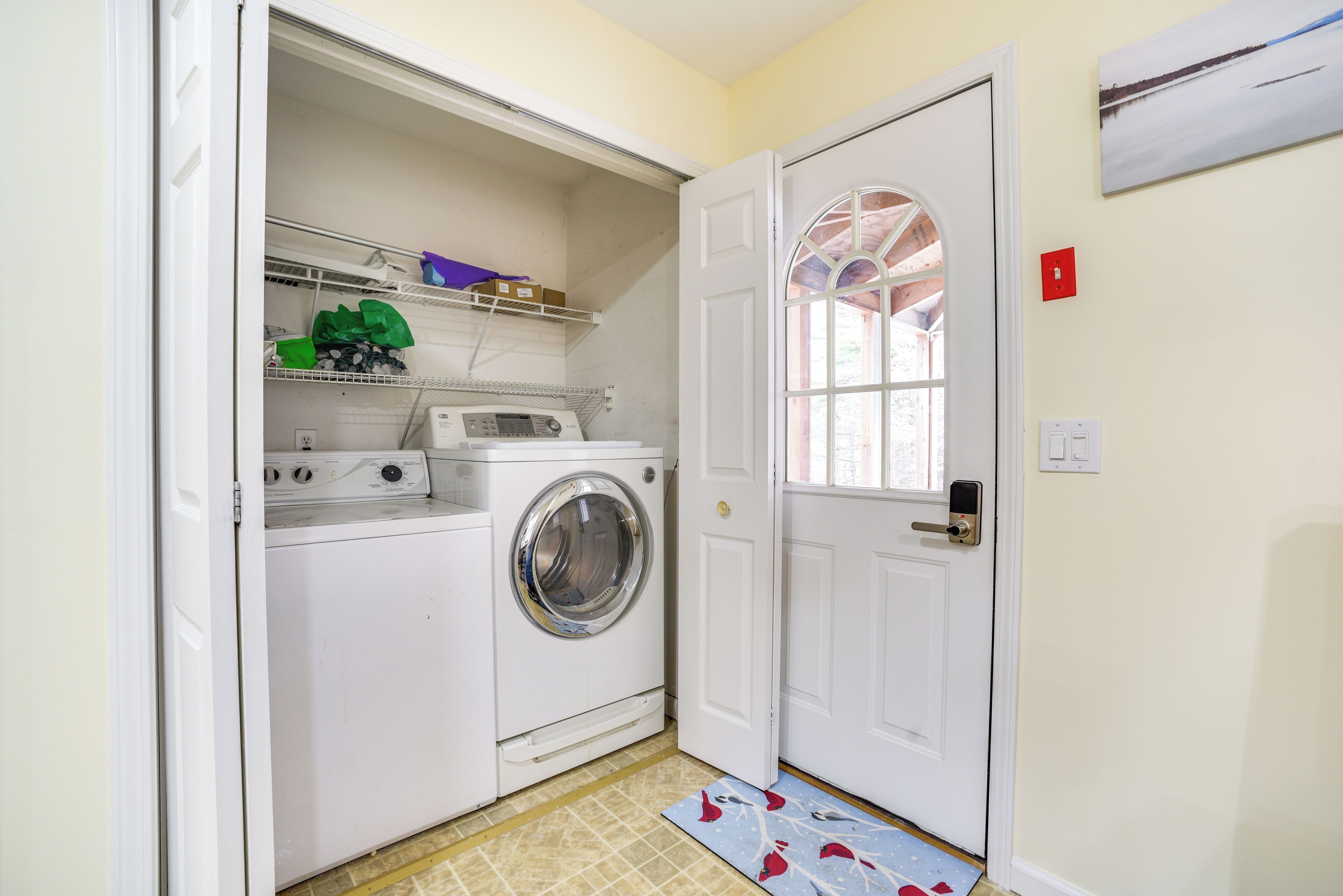 A laundry room with a washing machine and dryer, a small shelf with cleaning supplies, and a door with a window.