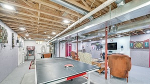Una mesa de ping pong en una habitación con vigas de madera a la vista, un dardo y una televisión.
