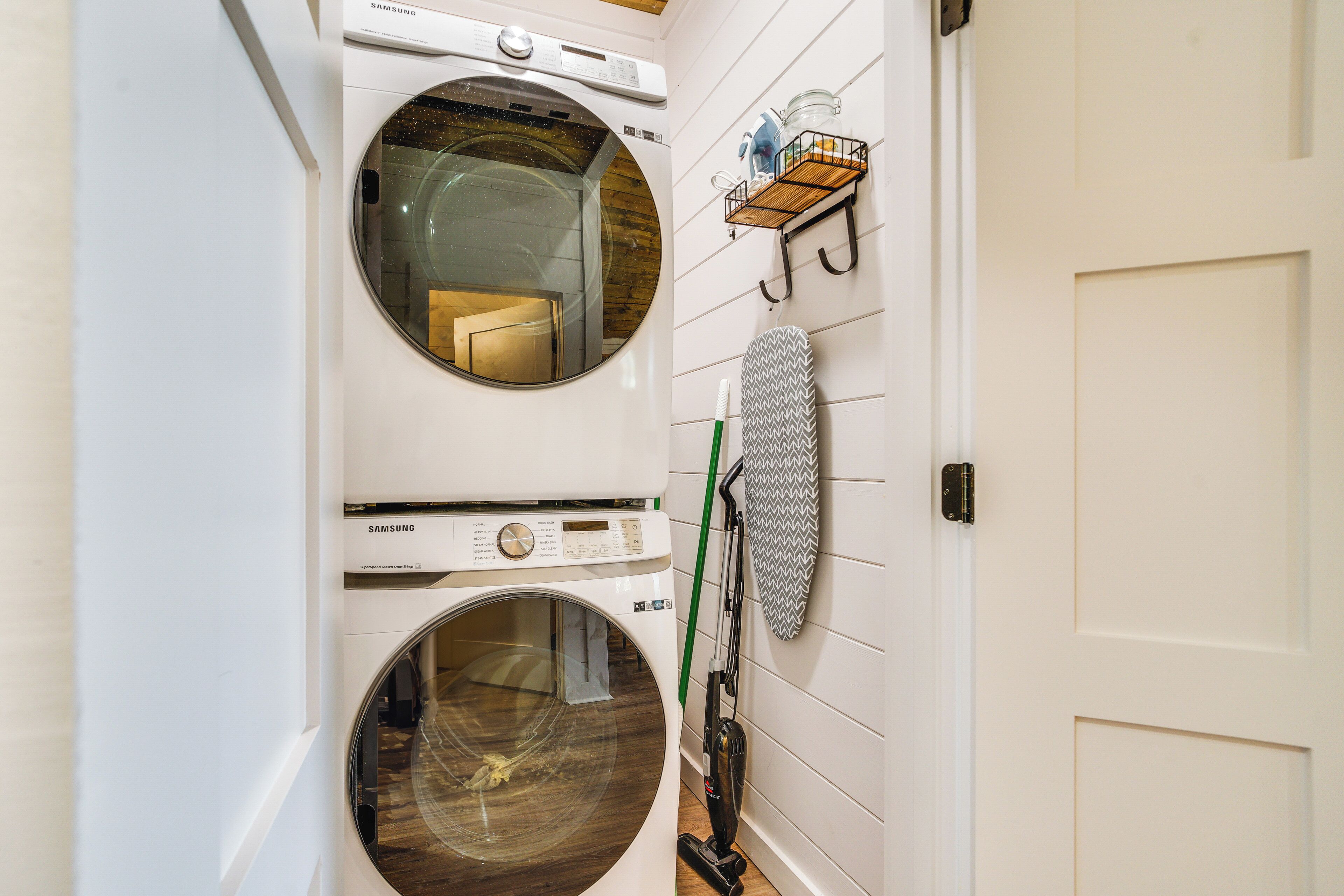 A laundry area with two front-loading washing machines, a hanging rack, and a vacuum cleaner.
