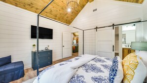 A bedroom with a wooden ceiling, a bed with patterned bedding, a dark dresser, a TV mounted on the wall, and a closet with sliding doors. - No Stairs Sleeps 10 Outdoor TV, Fire Pit, Pets (Broken Bow)