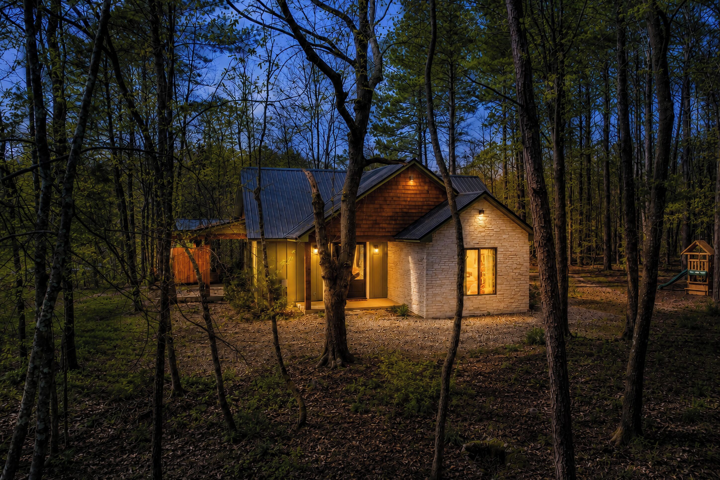 Une cabane aux murs en pierre, dotée d’une terrasse en bois et d’un toit en métal, entourée d’arbres.