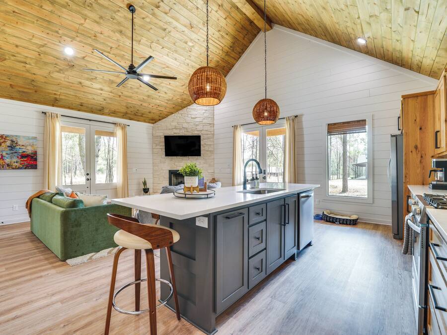 A spacious kitchen with a large island, wooden ceiling, and a green sofa in the living area.