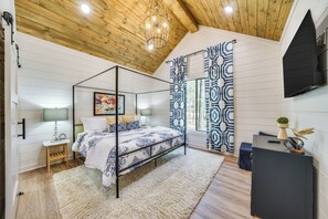Ein Schlafzimmer mit Himmelbett, Holzboden, Wand-Fernseher und Fenster mit gemusterten Vorhängen.