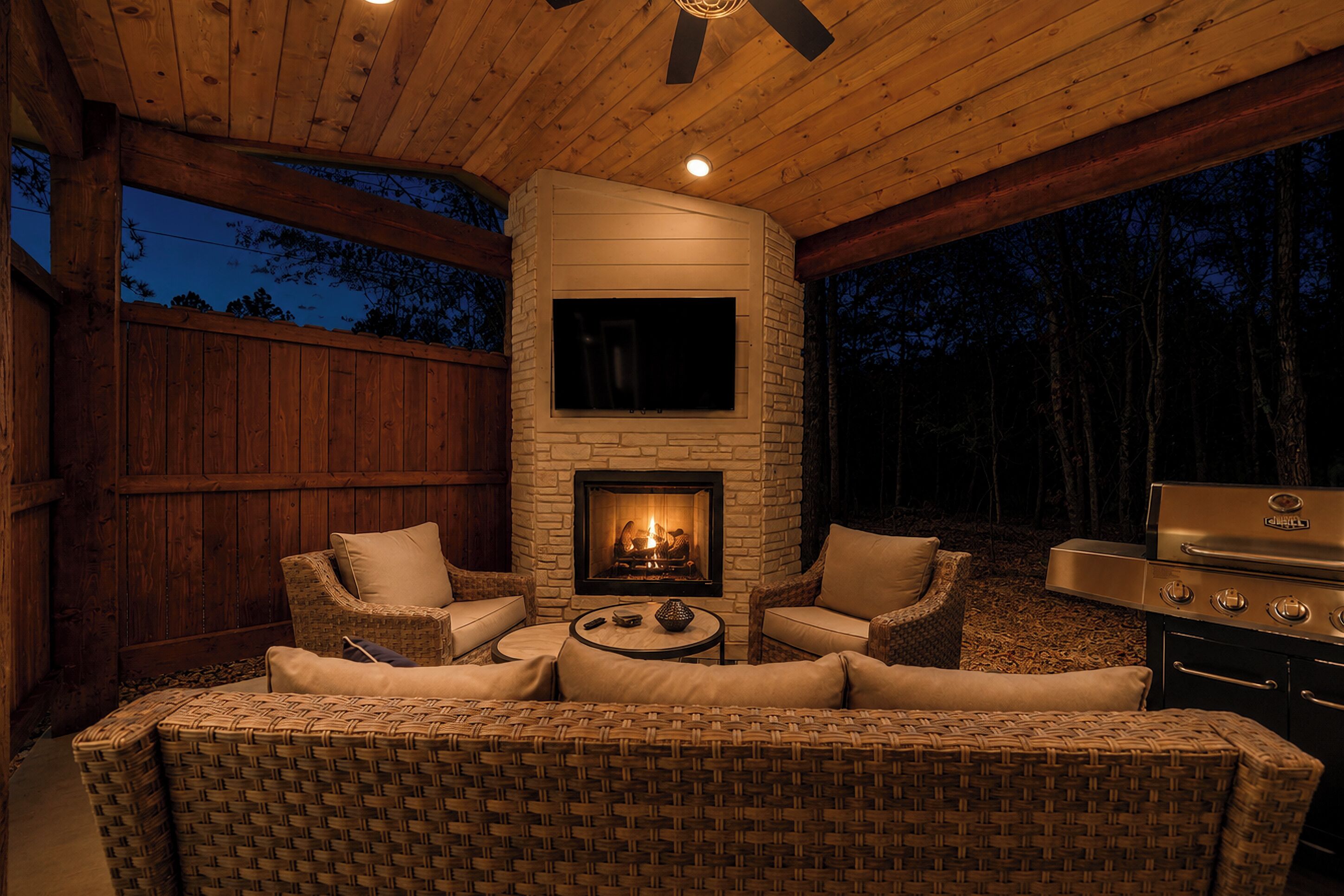 An outdoor patio with a stone fireplace, wicker furniture, and a grill.