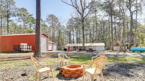 A rustic outdoor area with a brick fire pit, plastic chairs, and a red building.