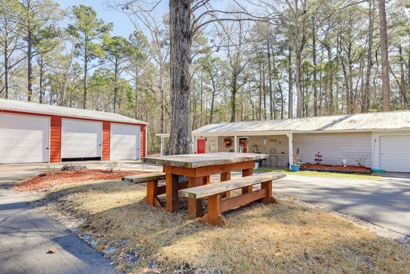 A rustic building with a large wooden picnic table in front, surrounded by a forest.
