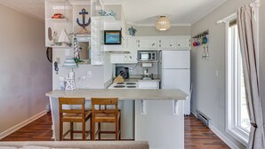 A compact kitchen with a central island, white cabinetry, and a small dining area with two chairs. - North Topsail Beach Condo w/ Ocean-view Balcony! (Sneads Ferry)