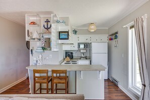A compact kitchen with a central island, white cabinetry, and a small dining area with two chairs. - North Topsail Beach Condo w/ Ocean-view Balcony! (Sneads Ferry)