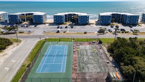 An aerial view of a coastal building complex with a tennis court, parking area, and ocean view. - North Topsail Beach Condo w/ Ocean-view Balcony! (Sneads Ferry)