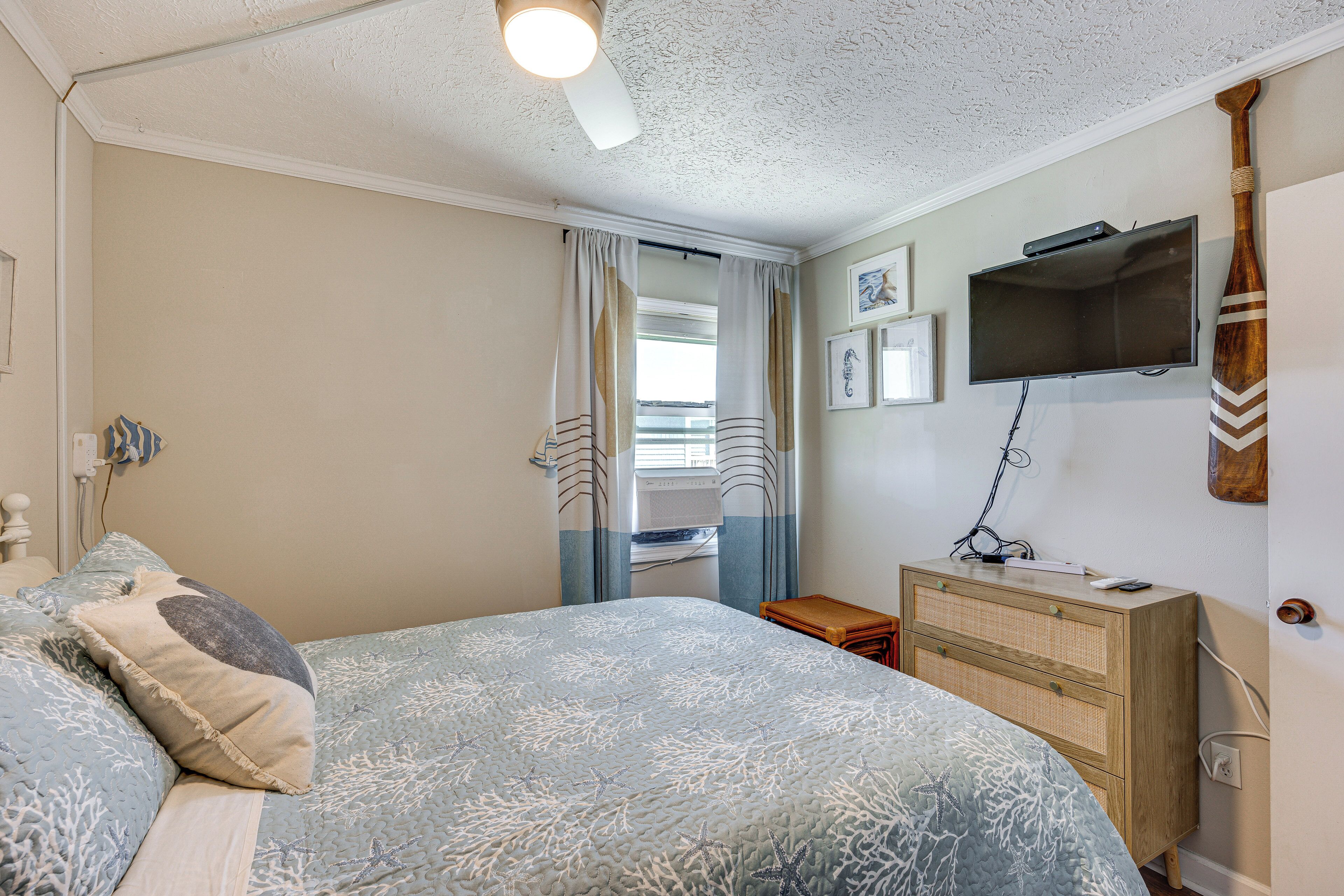Un dormitorio con cama, cómoda, televisor y ventana con cortinas.