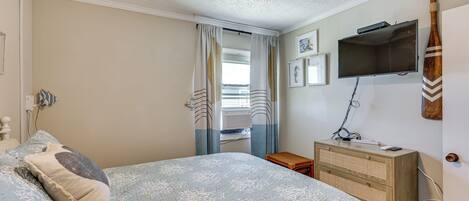 Un dormitorio con cama, cómoda, televisor y ventana con cortinas.