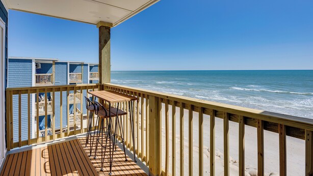 A wooden deck with a table and chairs overlooking the ocean. - North Topsail Beach Condo w/ Ocean-view Balcony! (Sneads Ferry)